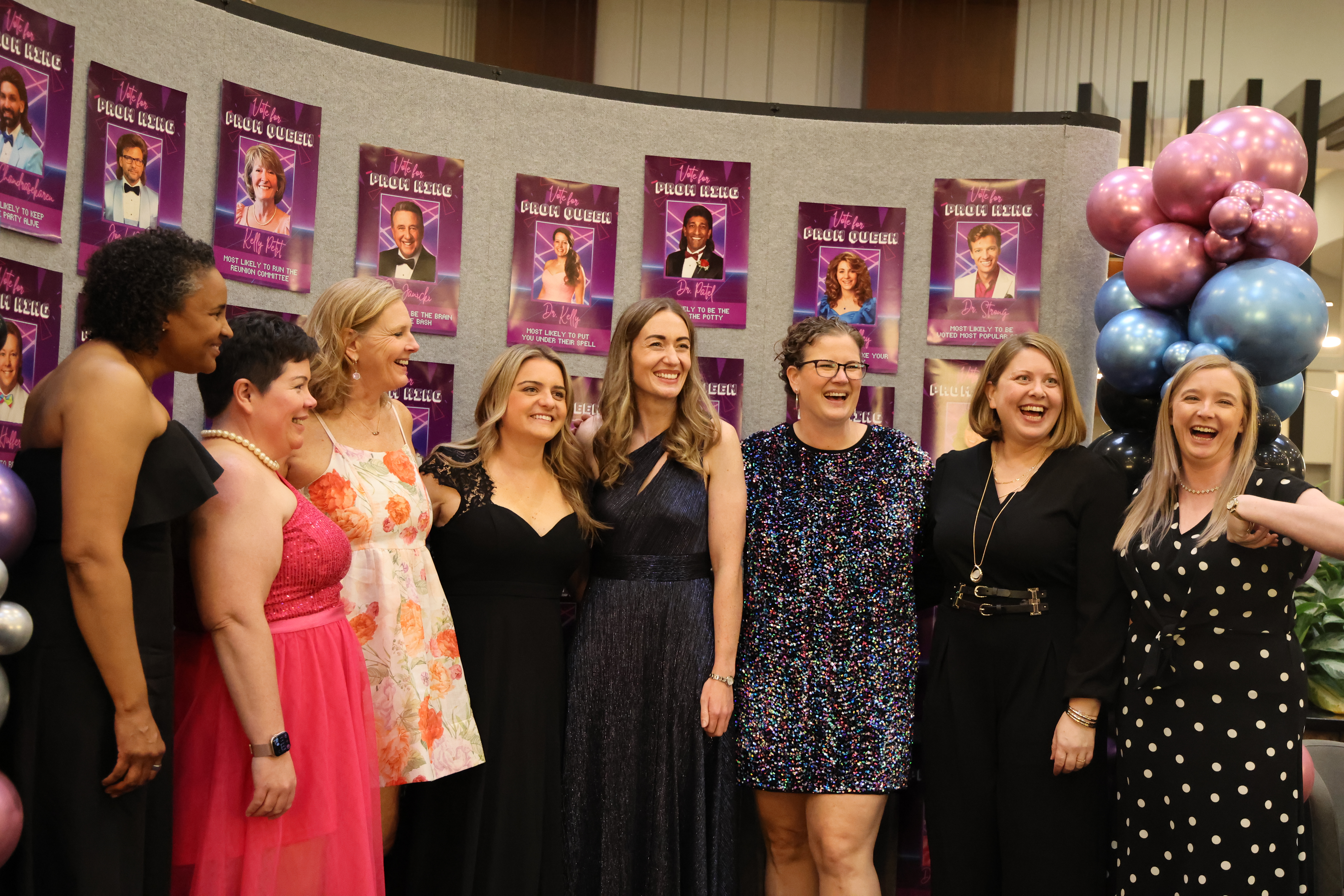 group of ladies posing in front of prom court wall