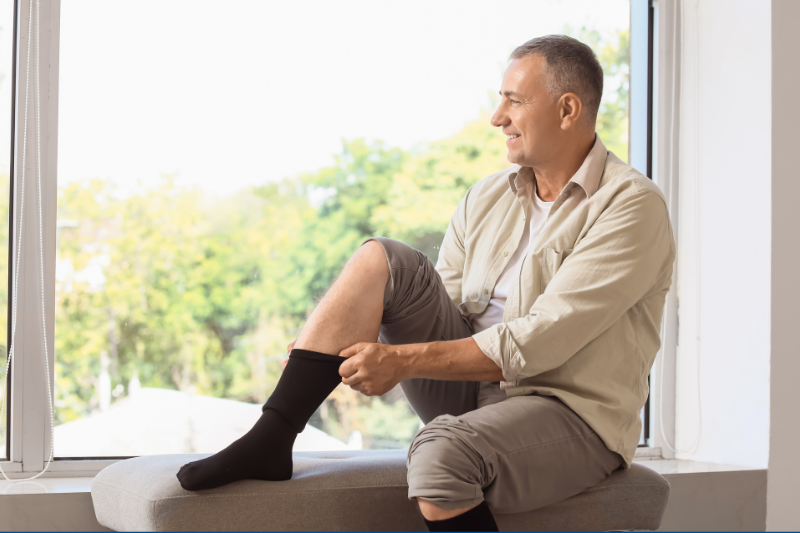 A man sitting on a window seat putting on compression socks